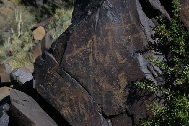 Group of people in the center. A vehicle. Rock drawings the Bayan-Zhurek.