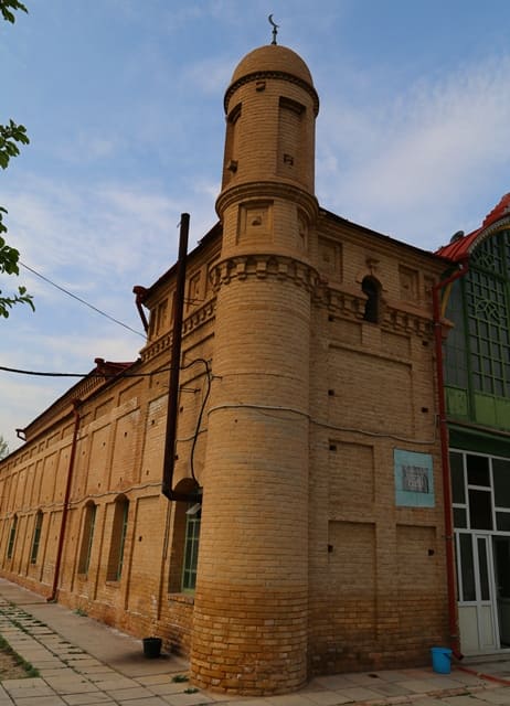 Nogai Ishan Mosque. The building's portal features a tall arch with a stained-glass window, flanked by two symmetrically built-in slender minarets. 2024