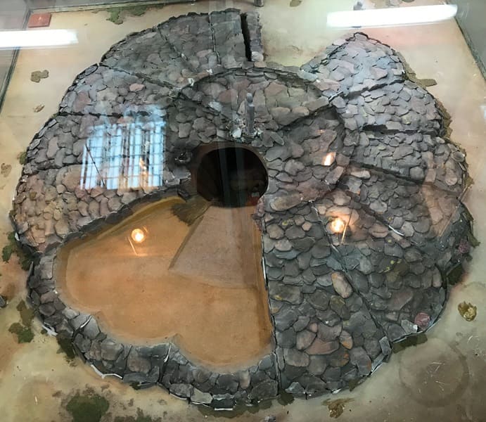 Model of the Araltobe burial mound. The Araltobe burial mound, explored by the West Kazakhstan archaeological expedition led by Professor Z. Samashev, dates back to the Sarmatian period. The site consists of three mounds with an earthen mound containing stone structures. The remains of a large man, apparently buried in full ceremonial attire, were found in the burial chamber of one of the mounds. The remains of a woman, two horses, a bird skeleton, and fragments of ceramic pottery were found nearby. Despite the mound being heavily looted, various ornaments and over three hundred gold plaques from ceremonial attire were found in the burial. The mound is circular, approximately 40 meters in diameter. The Araltobe structure above ground was a rounded structure covered in a scaly shell with 12 radial rays of vertical, buried slabs, likely representing the annual cycle.