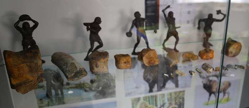 В витрине представлены бронзовые или металлические фигурки первобытных людей в различных позах, демонстрирующих охоту или повседневную деятельность.