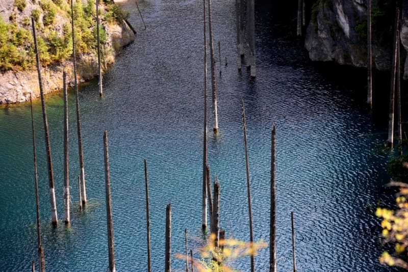 The landscape of Lake Kaindy is striking with its combination of rugged rocky slopes, coniferous forests, and the turquoise surface of this unique body of water.