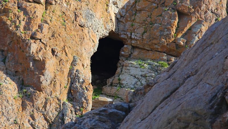 The entrance to the Aktogay Cave opens up among the overhanging cliffs.