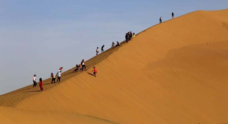 Каждый из туристов желает подняться на вершину песчаной горы.