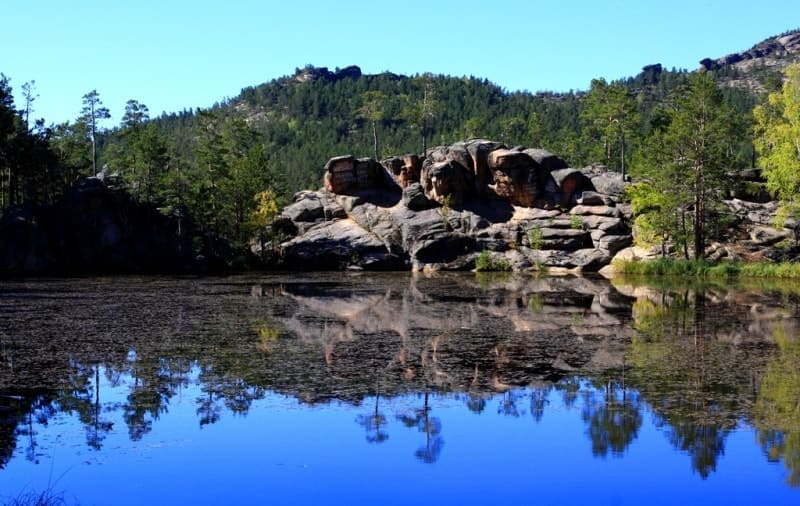 In calm weather, granite cliffs and trees surrounding lake are reflected in water.