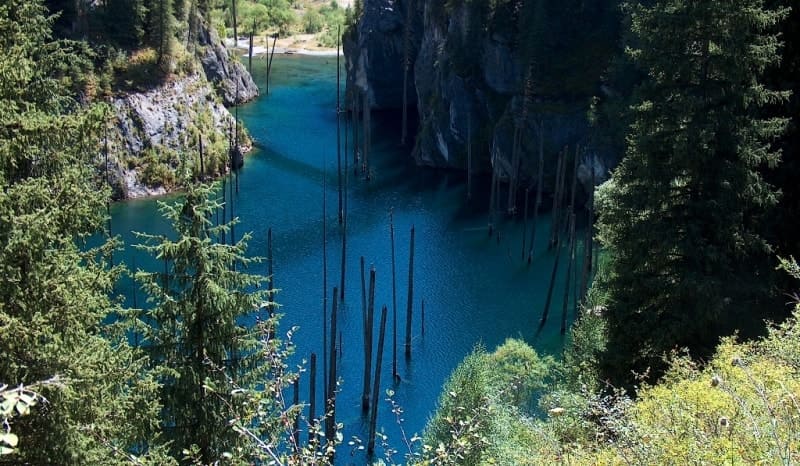 Бирюзовая гладь Каинды скрывает под собой затопленный лес, а высохшие стволы деревьев превосходят над водой словно тонкие свечи. Этот фантастический пейзаж - визитная карточка озера и один из самых узнаваемых его видов.