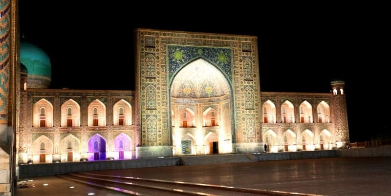 Interior of the architectural structure, the Tillya-Kari Madrasah. Blue and gold colors predominate, creating a "golden" interior effect. Arched openings with small windows decorated in the same style are visible. Natural light streams through the windows, highlighting the richness of the decoration.