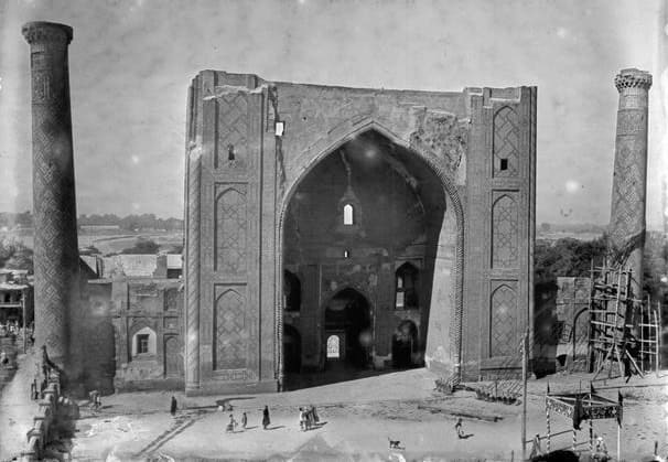 Photograph by Nikolai Vladimirovich Nekhoroshev, a renowned photographer who worked in Turkestan in the late 19th century. The photograph was taken between 1869 and 1871. It depicts the Ulugh Beg Madrasah in Samarkand in its original, unrestored form. At that time, the building was in a dilapidated state: the portal (peshtak) was severely damaged, and the wall cladding was missing in many places. Notably, the photograph does not yet show the engineering structures that were later used, in the early XXth century, to support the "leaning" northeastern minaret.